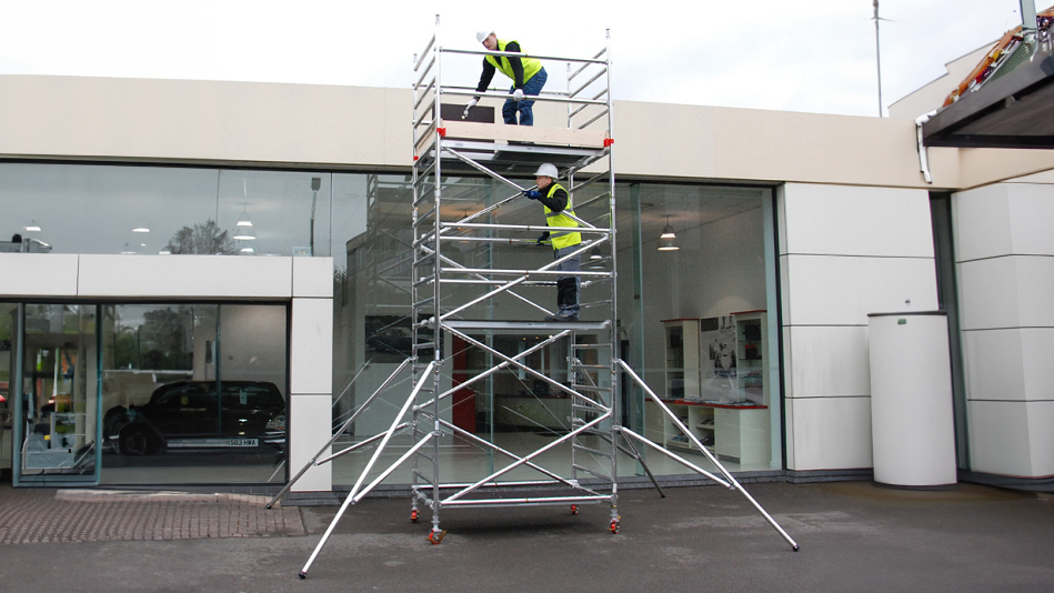 Worker ascending aluminum mobile tower on construction site